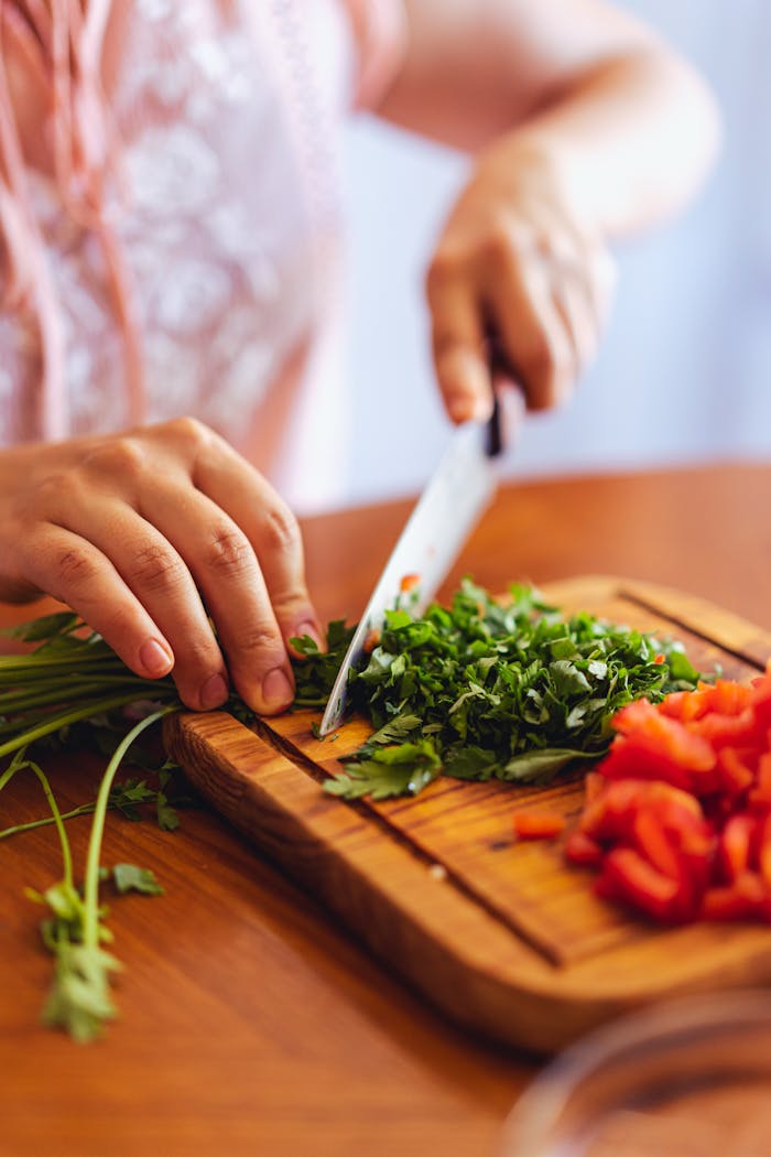 Fresh herbs and vegetables being chopped on a wooden board, showcasing culinary preparation.